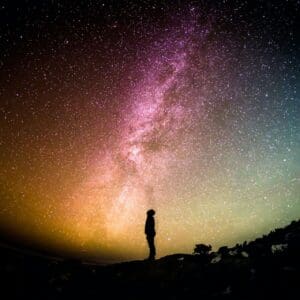 A person standing on top of a hill under a sky filled with stars.